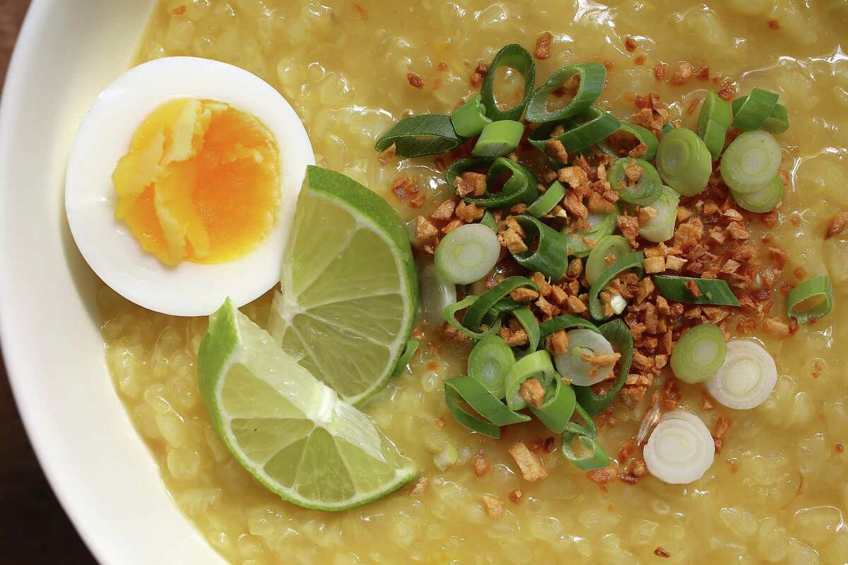 Arroz caldo, a Filipino congee, topped with boiled egg, lime wedges, scallions and fried garlic.