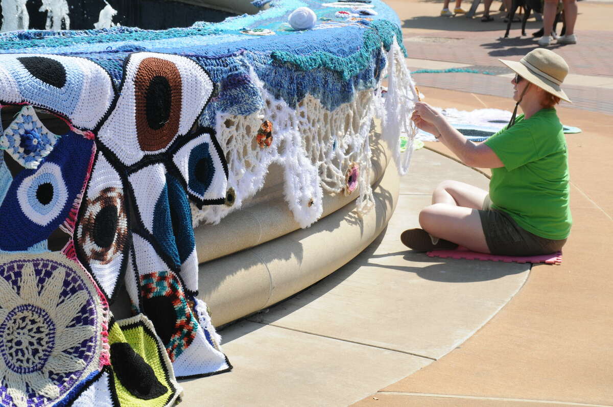 A member of the Riverbend Yarnbombers helps to adorn the Liberty Bank Amphitheater fountain with knitting during the Mississippi Earthtones Festival on Saturday.