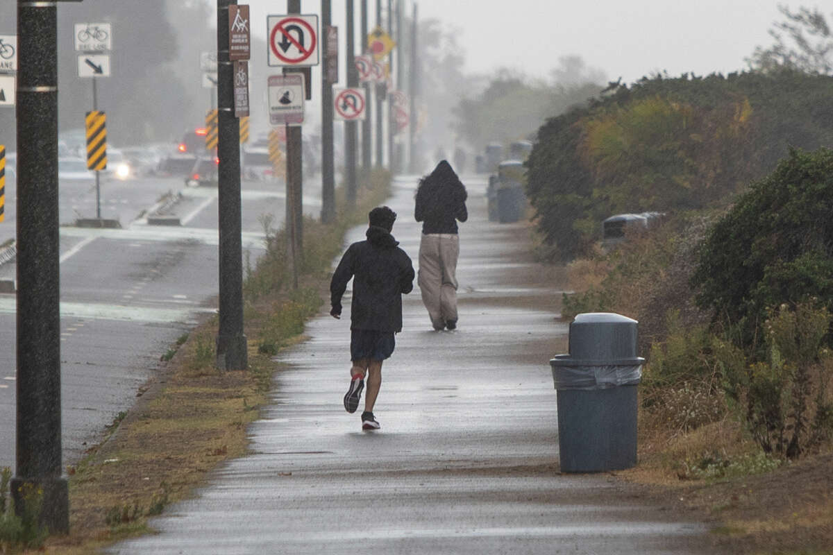 Pedestrians walk near Alameda Beach during heavy rain in Alameda, California on September 18, 2022.