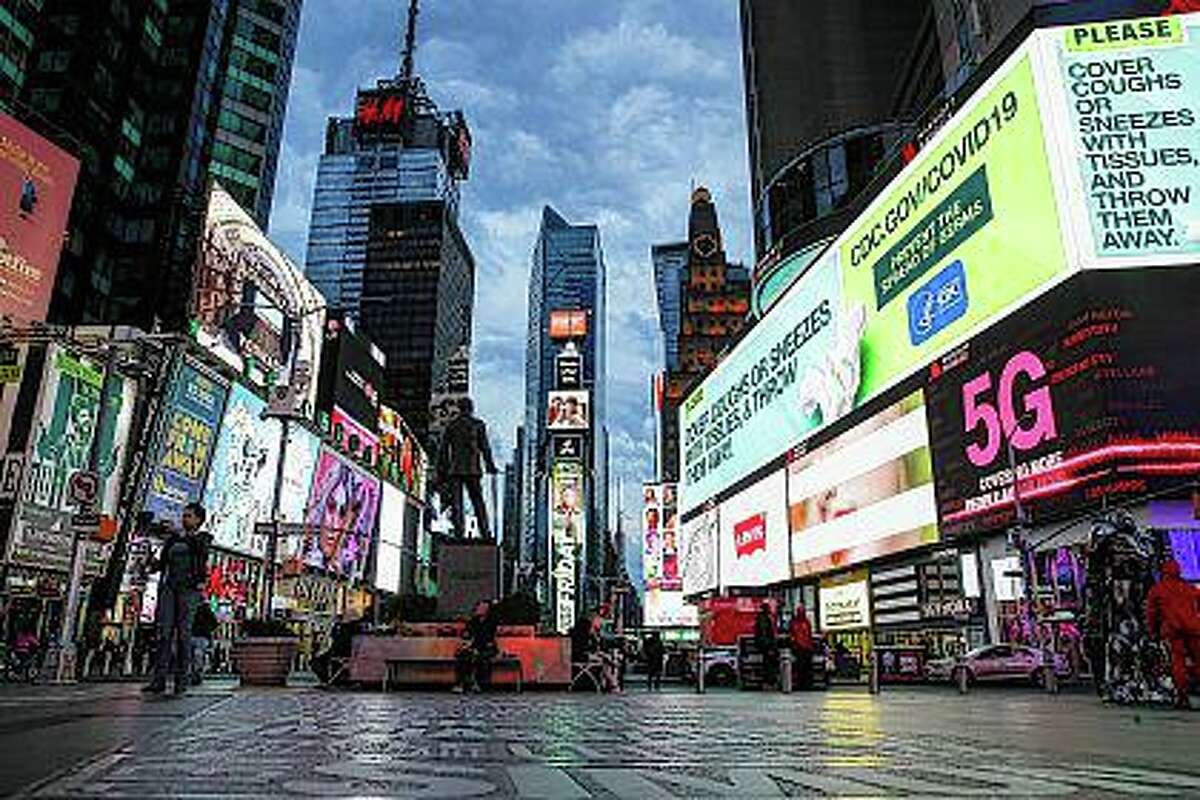 This March 20, 2020 file photo shows a screen displaying messages concerning COVID-19, right, in a sparsely populated Times Square in New York.