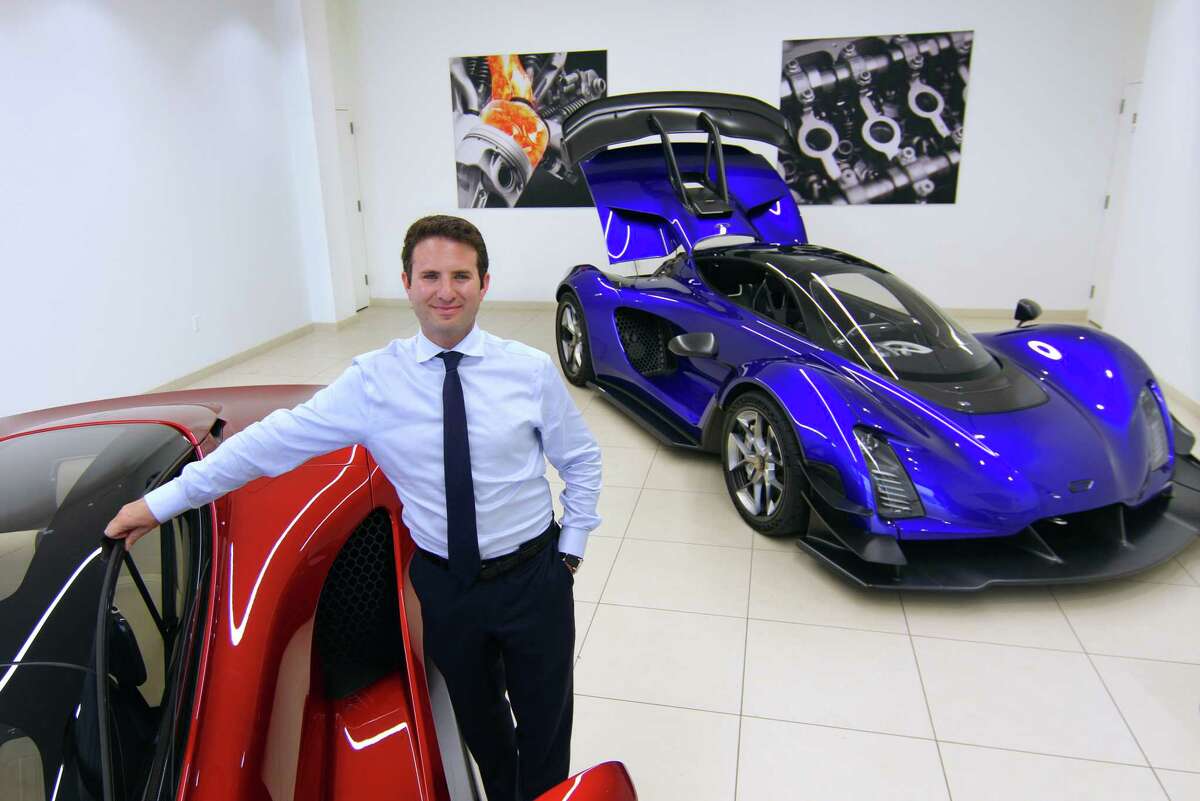 Evan Cygler, Brand Manager with Czinger Motors Greenwich, poses at Miller Motorcars with its two Czinger hypercars on display in their showroom in Greenwich, Conn., on Thursday September 22, 2022. The red Czinger is the new 21C V Max model. Designed and built in Los Angeles, the 21C (blue model) is currently the only vehicle on the planet designed and constructed using Czinger's progressive technological advancements.