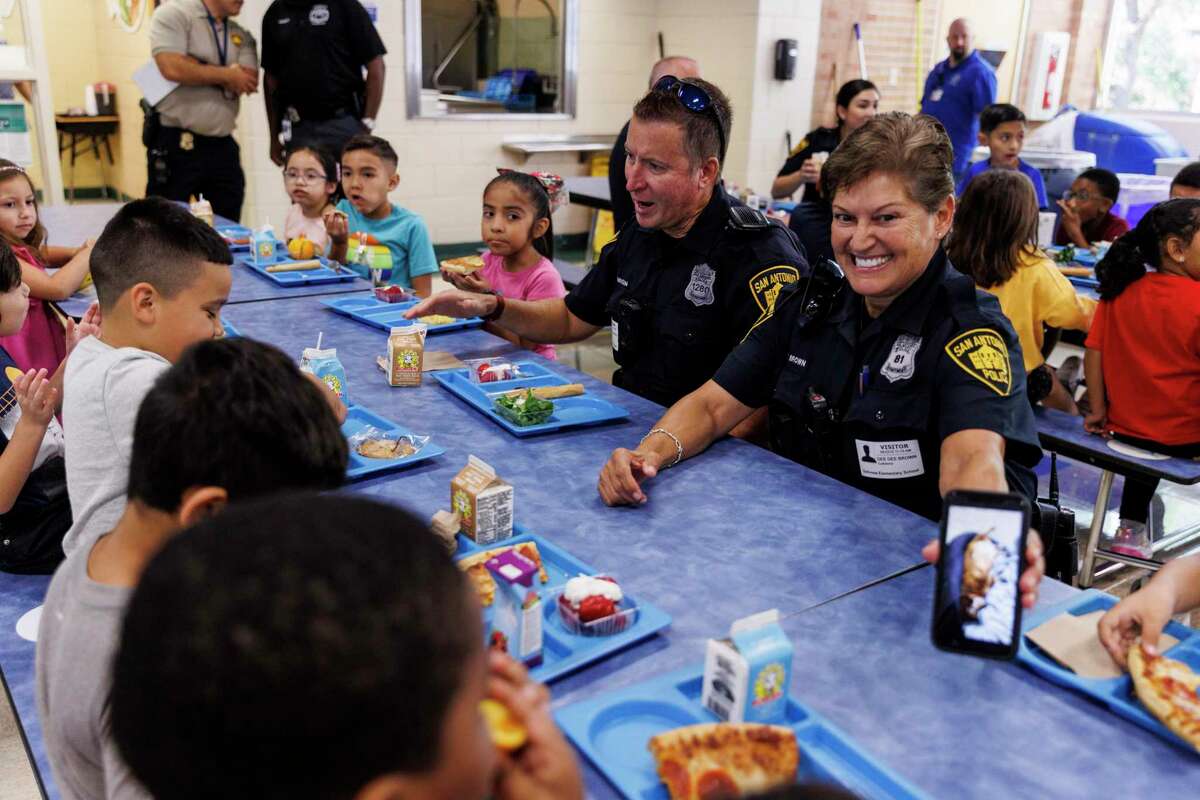 Officer Dee Dee Brown, right, shows a picture of a sleeping dog to children eating lunch as she, Officer Robert Henderson, left, and other SAPD officers spend their lunch break Thursday with students at Dellview Elementary.