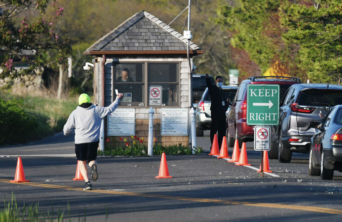 Cars line up at the gate as a jogger shows his park pass during the reopening of Greenwich Point Park in Old Greenwich, Conn. Thursday, May 7, 2020. A town investigation into an allegation against a Greenwich Point employee has resulted in that employee no longer working for the town and money being refunded. 
