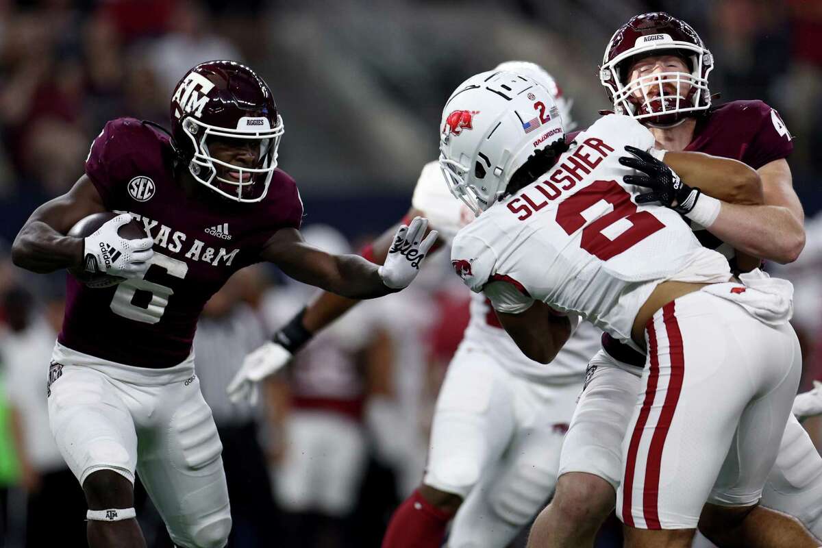 Texas A&M running back Devon Achane carries the ball against Arkansas defensive back Myles Slusher as tight end Max Wright blocks in the first half Saturday’s game in Arlington.