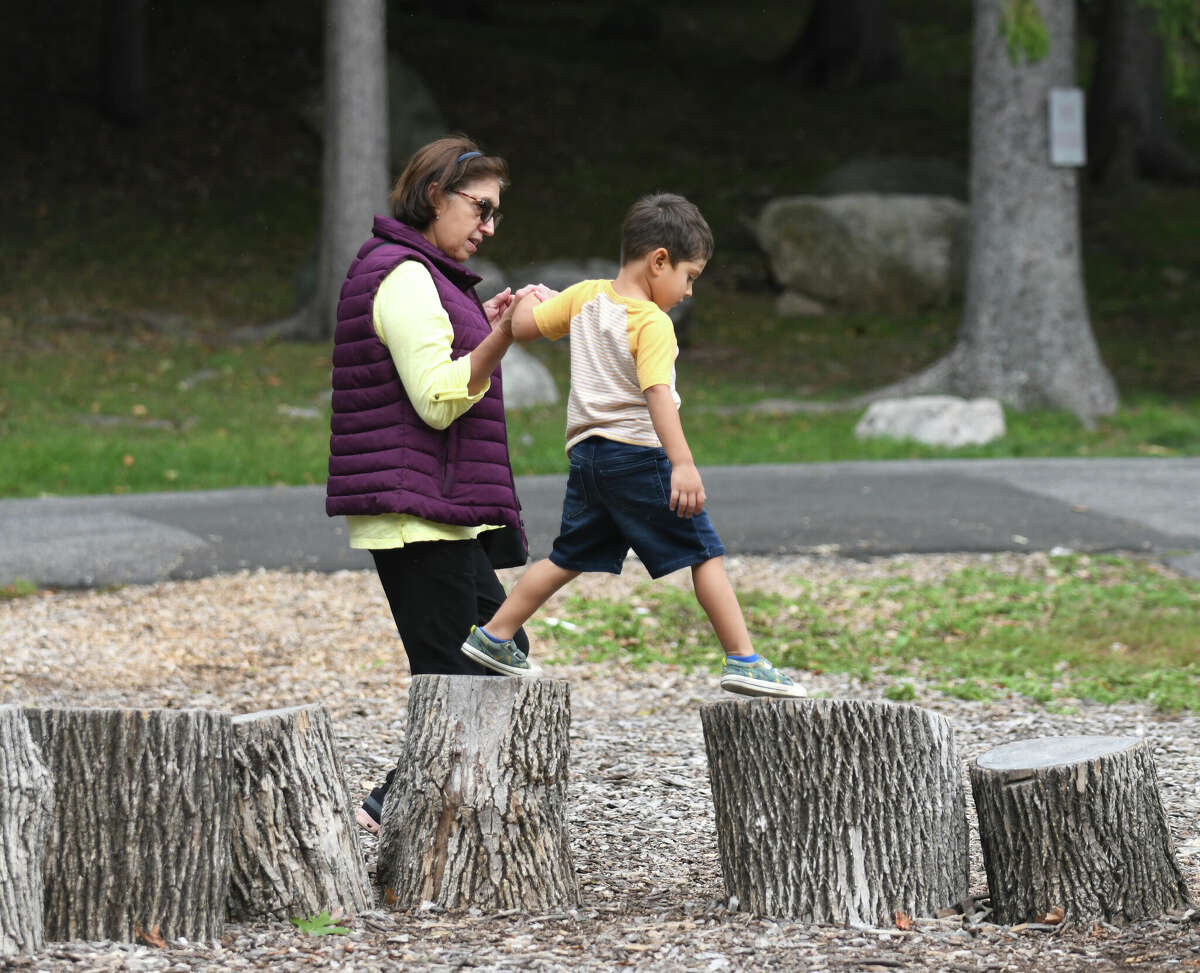 Amparo Mejia, of Mamaroneck, NY, holds hands with 4-year-old Lucious Alfano while walking on tree stumps during Fall Family Fest Sundays at the Stamford Museum & Nature Center in Stamford, Conn.  Sunday September 25, 2022. The children's event featured a climbing wall, a birds of prey program, live music, face painting, games, crafts and an apple slingshot.  Fall Family Fest continues October 2 and 9 from 10 a.m. to 2 p.m. with online pre-registration recommended.