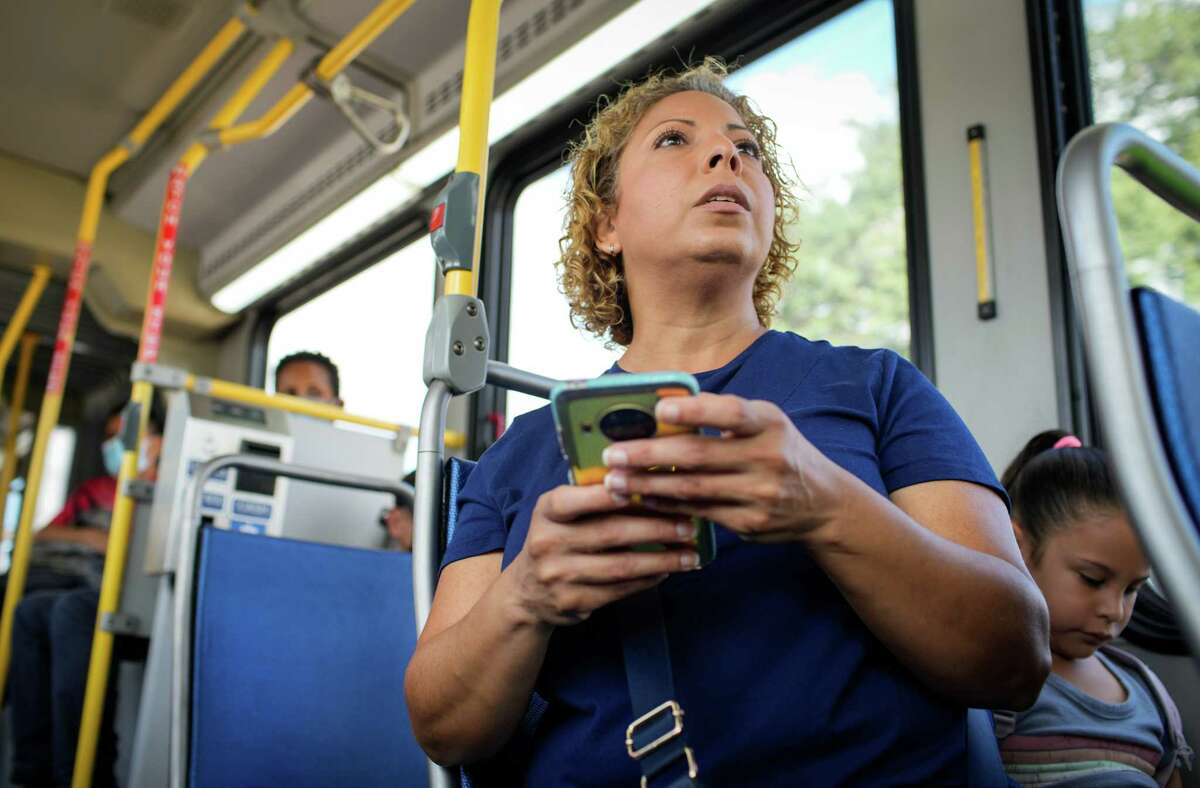 Glory Medina checks her phone as she rides a bus in Houston. She sometimes spends hours every day traveling  by bus, often at unsheltered stops.