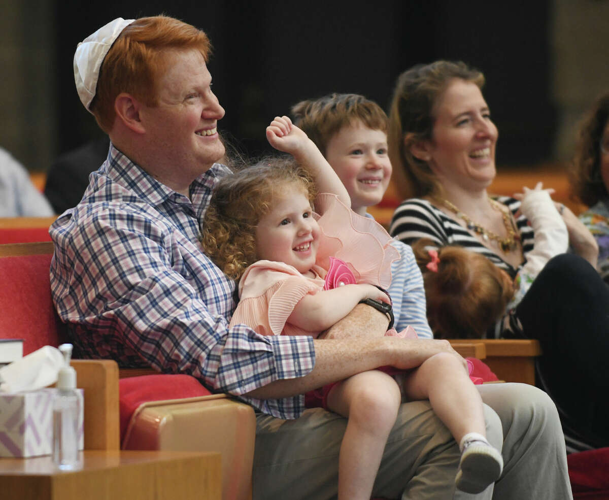 Jeffrey and Julia Horowitz, along with their children, Arielle, 3, Charles, 5, and Lily, 10 months, smile during a song at the Tot Holidays Rosh Hashana program at Temple Sholom in Greenwich, Conn. Monday, Sept. 26, 2022. Artist-in-residence Sheldon Low led children and their families in prayer and song to introduce youngsters to the Rosh Hashana holiday.