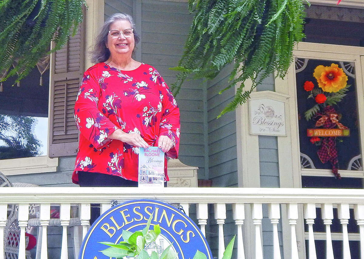 Innkeeper Gwenn Eyer stands on the porch of her Blessings on State Bed and Breakfast, holding a copy of Rachael Bloome's latest novel, "Blessings on State Street." The book drew on the bed and breakfast and the Eyer family's story as inspiration.