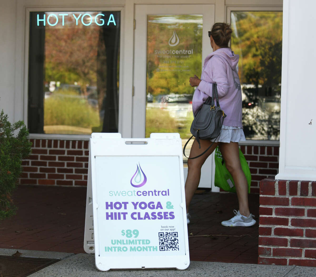 A sandwich board and neon sign are displayed outside Sweat Central yoga studio in Darien, Conn. Tuesday, Sept. 27, 2022. After relaxing the rules during the pandemic, Darien officials plan to resume enforcement of storefront regulations that prohibit banners, sandwich board signs, and signs on street posts.