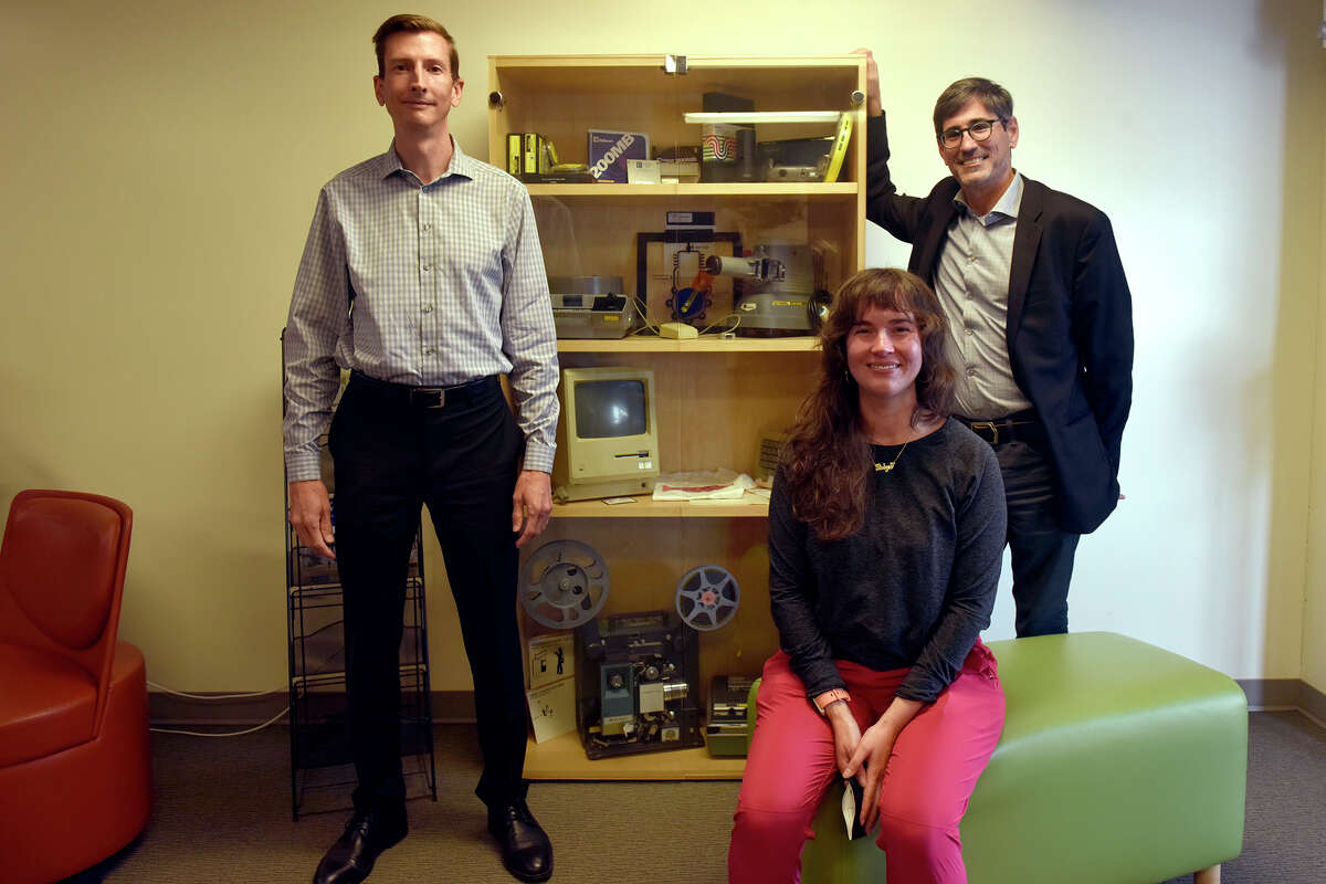 From left, Daniel Johnson, Robyn Ollodort, and Andrew Roderick are pictured in SFSU's Department of Academic Technology next to a display cabinet of various tech relics.