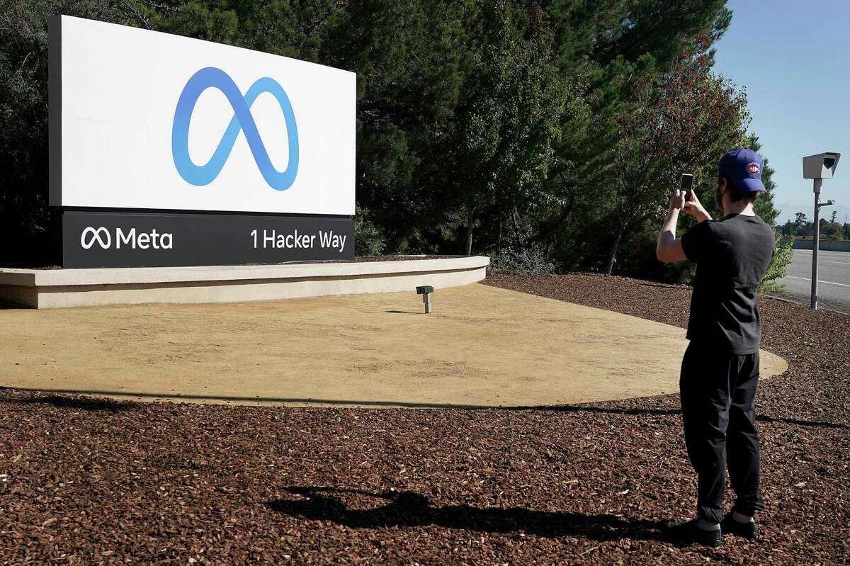A Facebook employee takes a photo in front of the Meta Platforms Inc. sign outside the company headquarters in Menlo Park, Calif. The company said it plans to institute a hiring freeze.