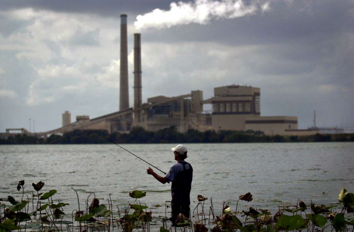 Emissions rise from the smokestack at the J.K. Spruce Power Plant as David Foster fishes at Calaveras Park in this 2003 file photo.