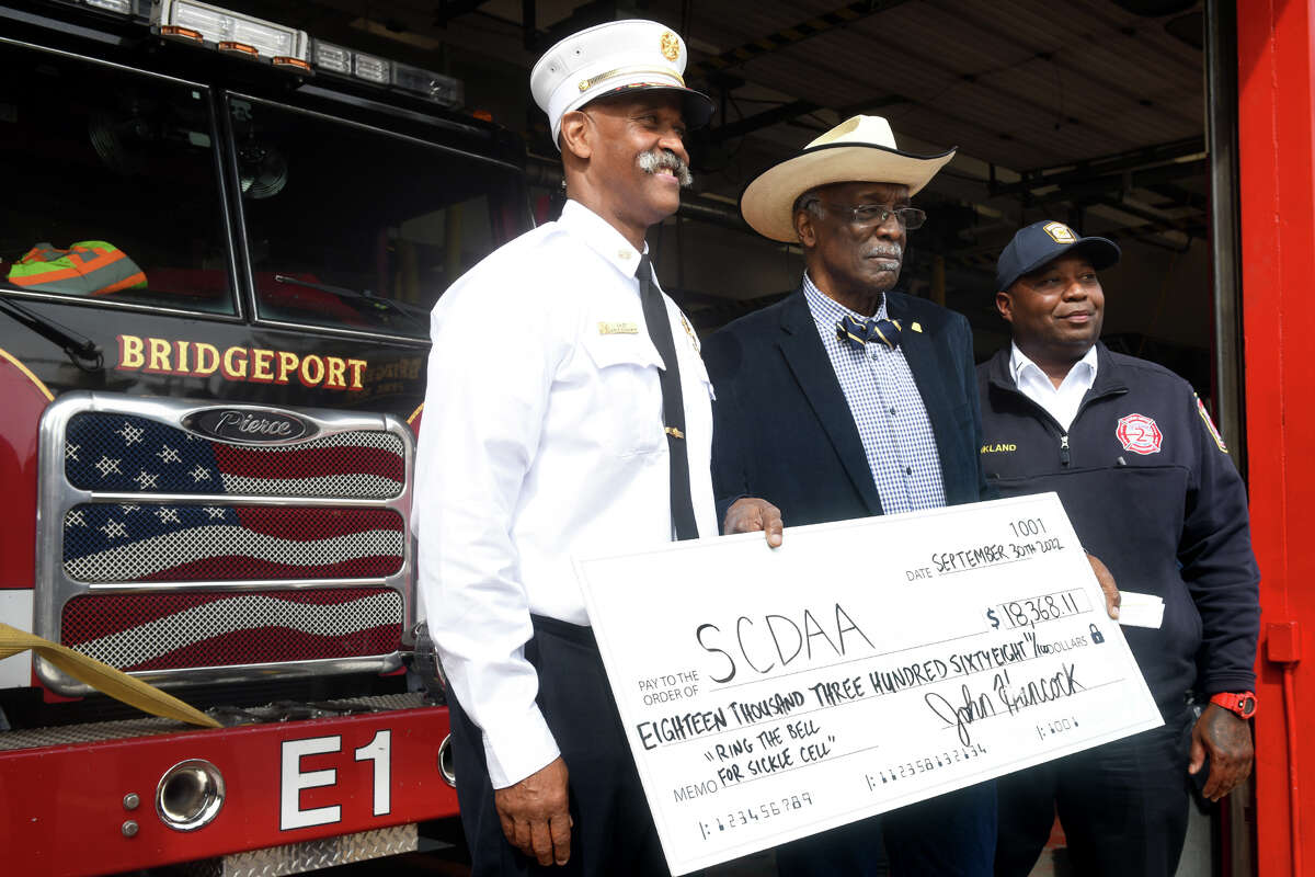 From left, Acting Fire Chief Lance Edwards, James Rawling, President and CEO of Sickle Cell Disease Association of American, Connecticut, and Fire Lt. Joe Kirkland, President of the Bridgeport Firebirds, stand together during a check presentation at fire headquarter, in Bridgeport, Conn. Sept. 30, 2022. Members of the Bridgeport Fire Department collected over $18,000 for SCDAA during recent “Ring the Bell for Sickle Cell” boot drives.