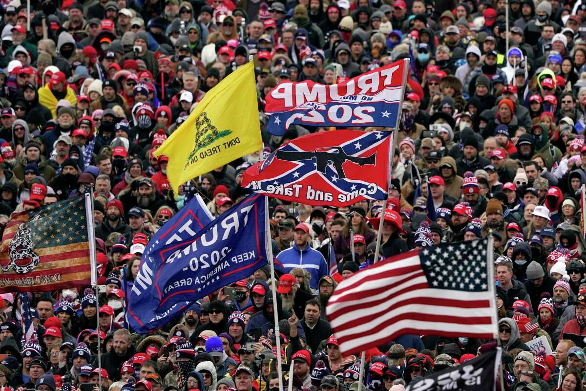 In this Wednesday, Jan. 6, 2021, photo, supporters listen as President Donald Trump speaks as a Confederate-themed flag and other flags flutter in the wind during a rally in Washington.