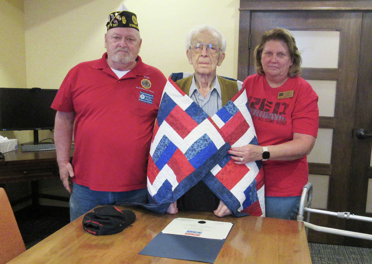 Mike Lombardi, middle, a 100-year-old World War II veteran who is a resident at Stillwater Senior Living in Edwardsville, is flanked by Al Mahan from Venice-Madison American Legion Post 307 and Jan Copeland from Quilts of Valor as he receives a quilt for his service.