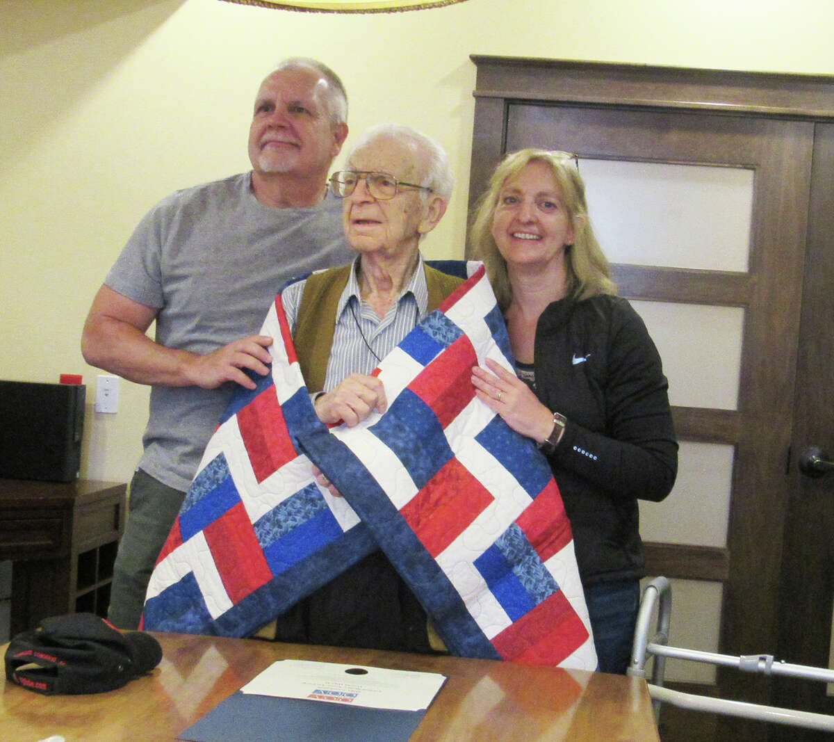 Mike Lombardi, middle, a 100-year-old World War II veteran who is a resident at Stillwater Senior Living in Edwardsville, is flanked by his son, James Lombardi, and his daughter, Michele Grieve, as he receives a quilt from Quilts of Valor.