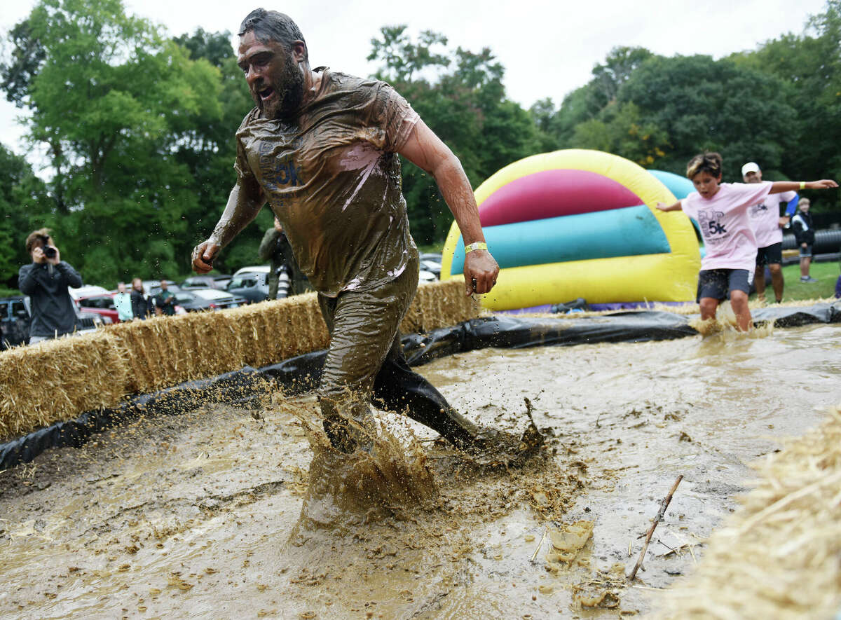 Greenwich's Phil Schacter is drenched in mud as he crosses the finish line in the 10th annual Boys & Girls Club of Greenwich Muddy Up 5K run at Camp Simmons in Greenwich, Conn. Sunday, Oct. 2, 2022.