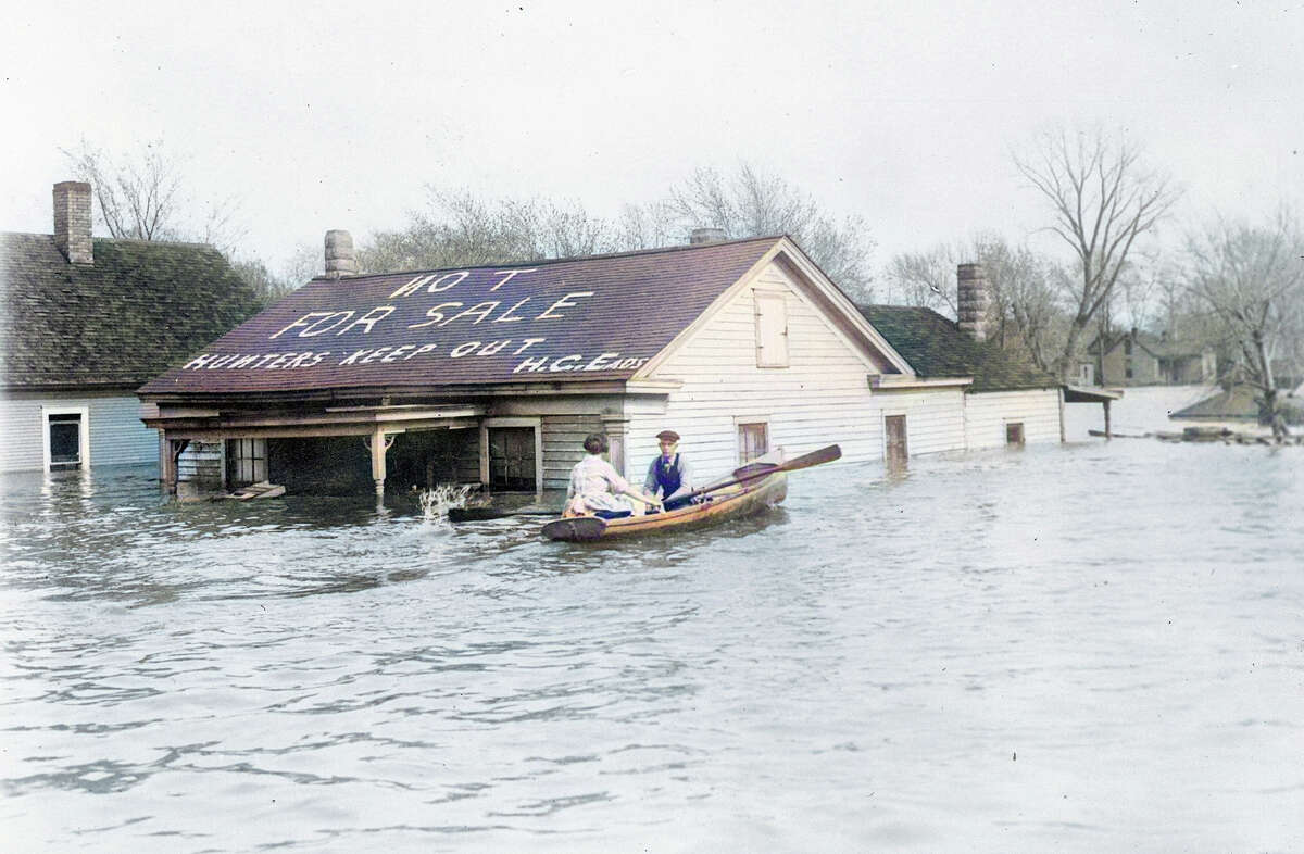 A man and woman row along a flooded street in Beardstown during flooding in 1922. A message left on the roof of a flooded house by homeowner H.C. Eads reads, "Not For Sale. Hunters Keep Out."
