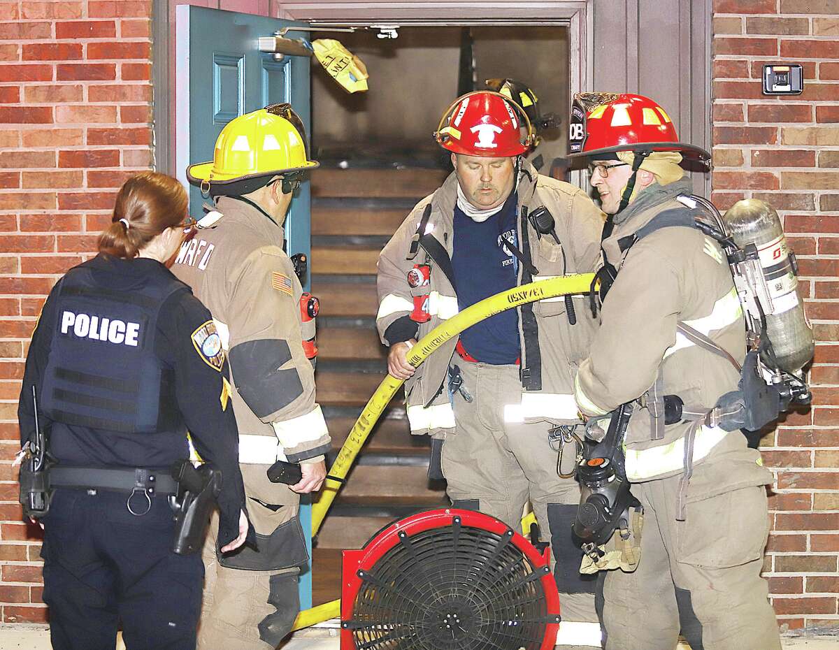 John Badman|The Telegraph Firefighters withdraw a hose from the entrance to Units 7-12 of the Metro Apartments of Wood River early Monday morning. An exhaust fan was used to clear smoke from the stairwell of the building.
