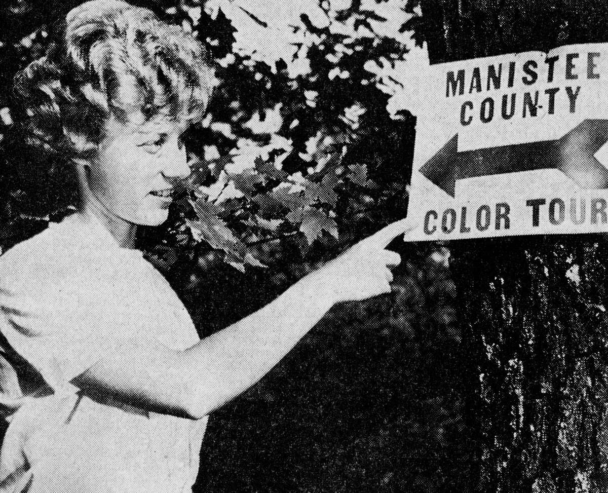 Manistee County's fall colors are at an almost incredible intensity and barring bad weather, should exist for another week or so. Judy Carlson of the Manistee County Board of Commerce points out one of the many color tour signs put up by the board. The photo was published in the News Advocate on Oct. 8, 1962.
