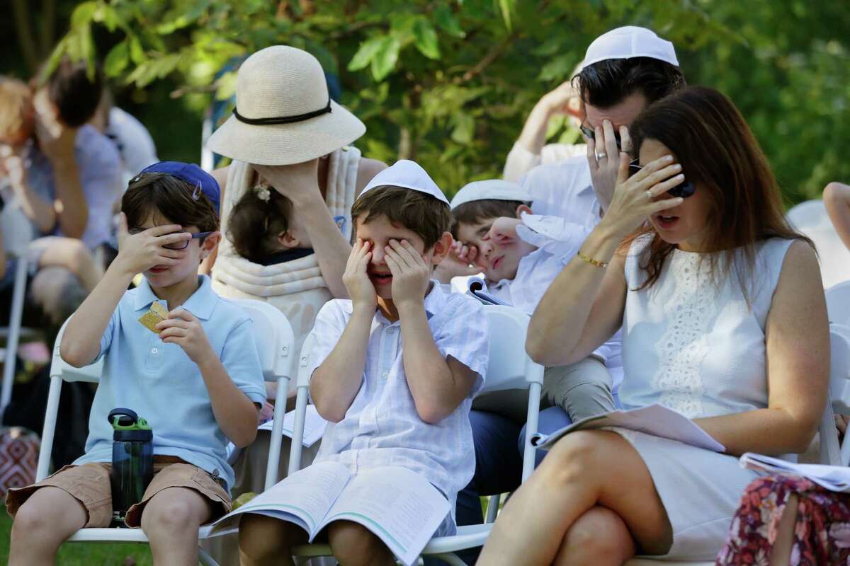 Parents and their kids cover their eyes as they sing a song during a service Wednesday in the observance of Yom Kippur by members of Congregation Brith Shalom at the Nature Discover Center.