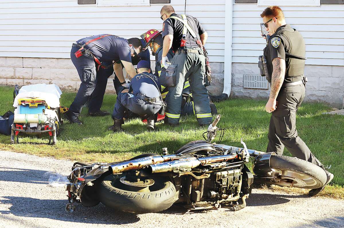 John Badman|The Telegraph Alton firefighters and pramedics work on a man in serious condition Saturday at Milton Road and Franor Street after he lost control of his motorcycle, left the roadway and ended up in the yard of a house.