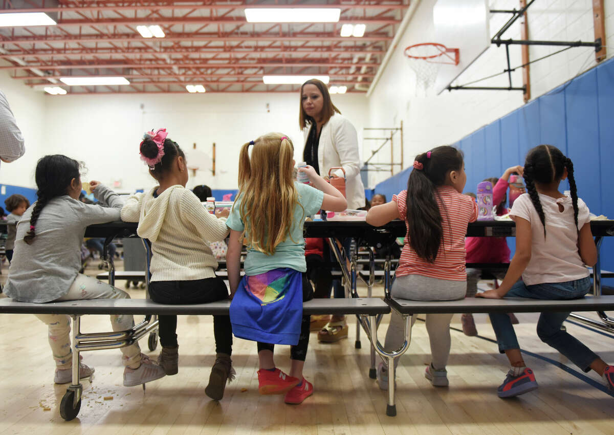 Kindergarten paraprofessional Sarai Cruz chats with students eating lunch at Newfield Elementary School in Stamford, Conn. Thursday, Oct. 6, 2022. Stamford recently qualified for a state program that allows the district to offer lunch for free to all students for the next four years. The program reimburses the district for meal costs, but the district could get an even higher reimbursement in the future if more families sign up for programs like SNAP and HUSKY.