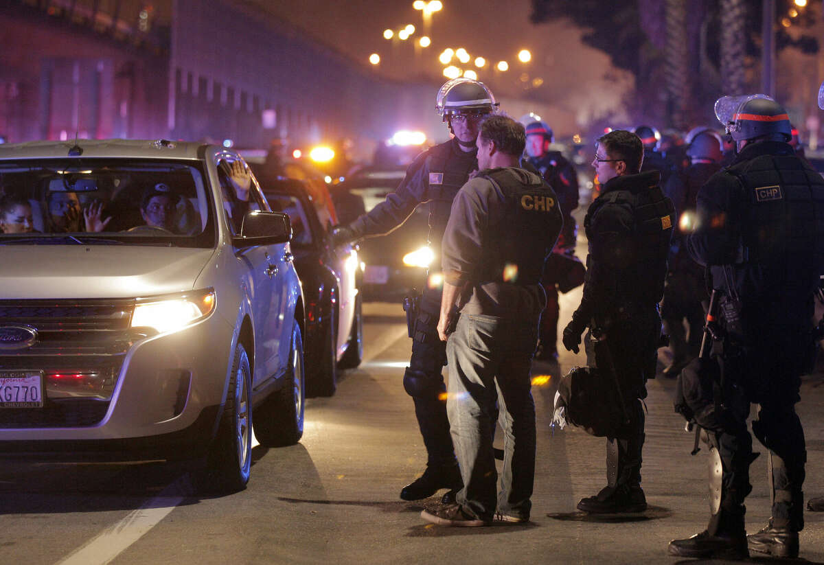 A driver and his passenger hold their hands up while they wait to be processed for citation and released after Bay Area officers raided a large sideshow event in November 2014.
