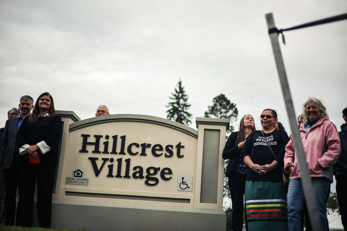 Around a dozen people take a group picture in front of the Hillcrest Village apartments sign on Thursday in Manistee. 