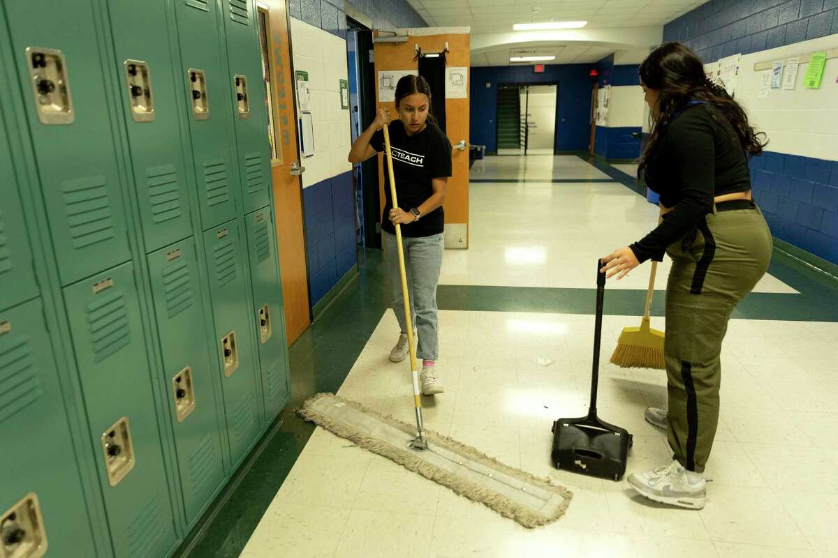 Brisa Rico and Monica Saldana sweep a second floor hallway at MacArthur High School on Thursday, part of a program that helps keep the school clean — now a necessity rather than a good will gesture, because of a severe custodian shortage throughout NEISD. Each afternoon around 15 students sweep and change trash bags, saving hours of work for two custodians.