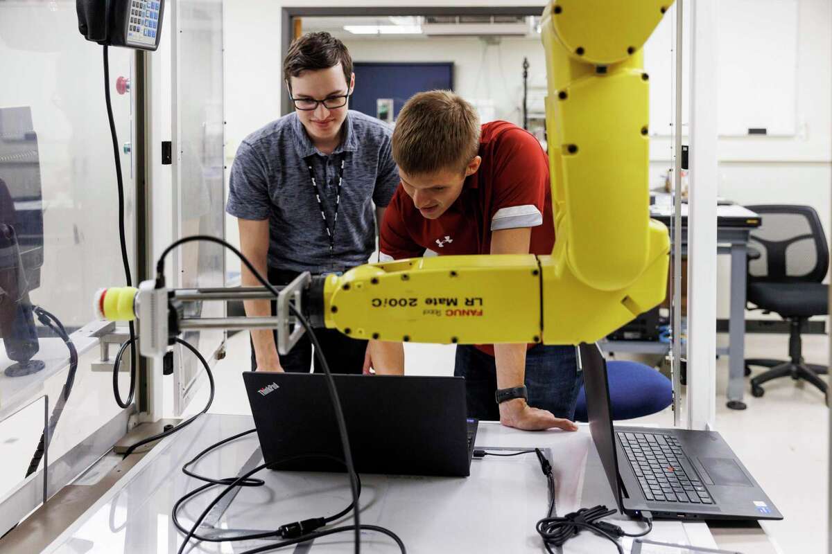 Research engineers David Spielman, left, and Tyler Marr work together to program the FANUC robot for a demonstration project at the Southwest Research Institute.