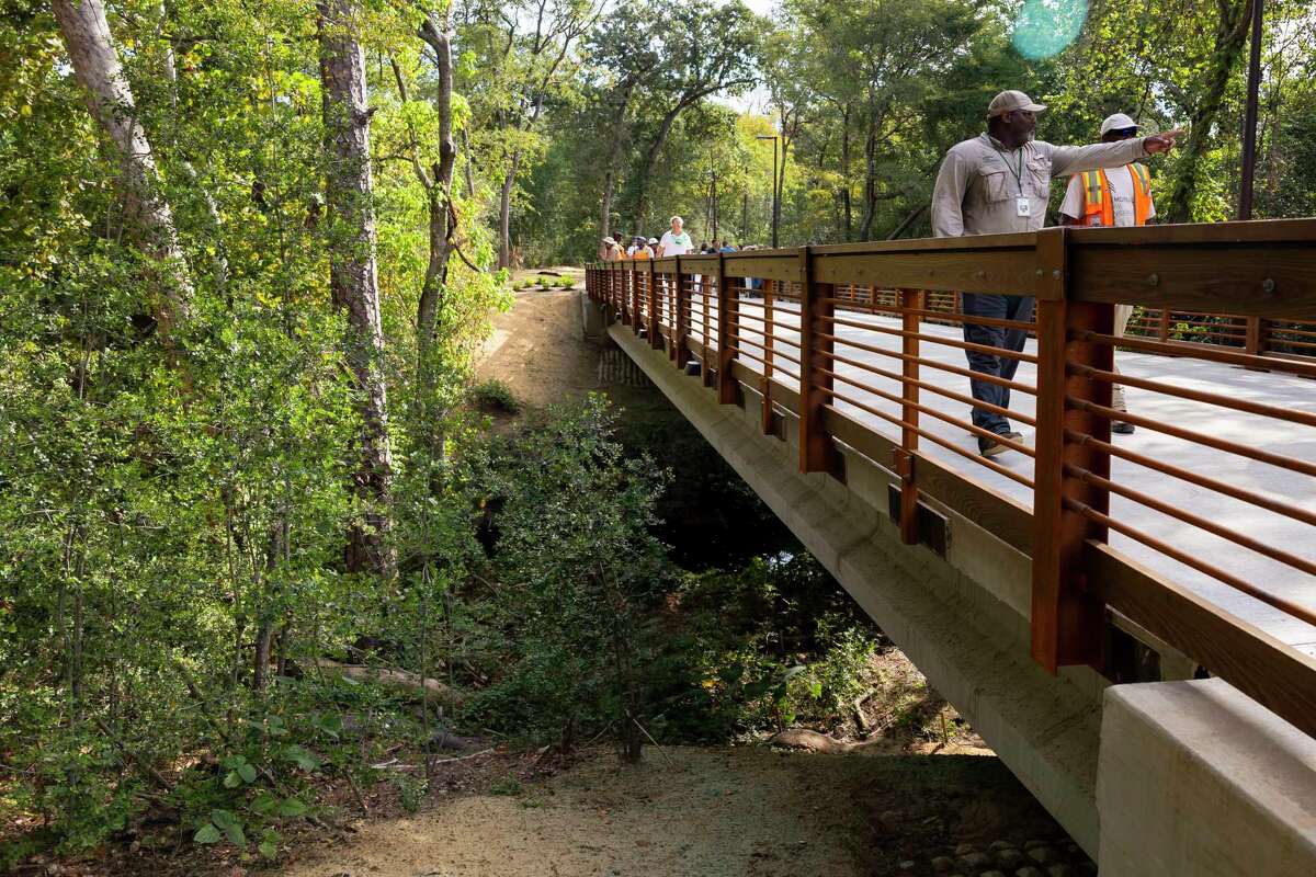 Theo White, a member of the grounds department at MPC, walks over one of the new bridges during the opening of a new section of the Seymour Lieberman Trail at Memorial Park on Friday, Oct. 7, 2022. The newest section diverts runners off of the sidewalk along Memorial Drive to a new, shaded trail with three pedestrian bridges.