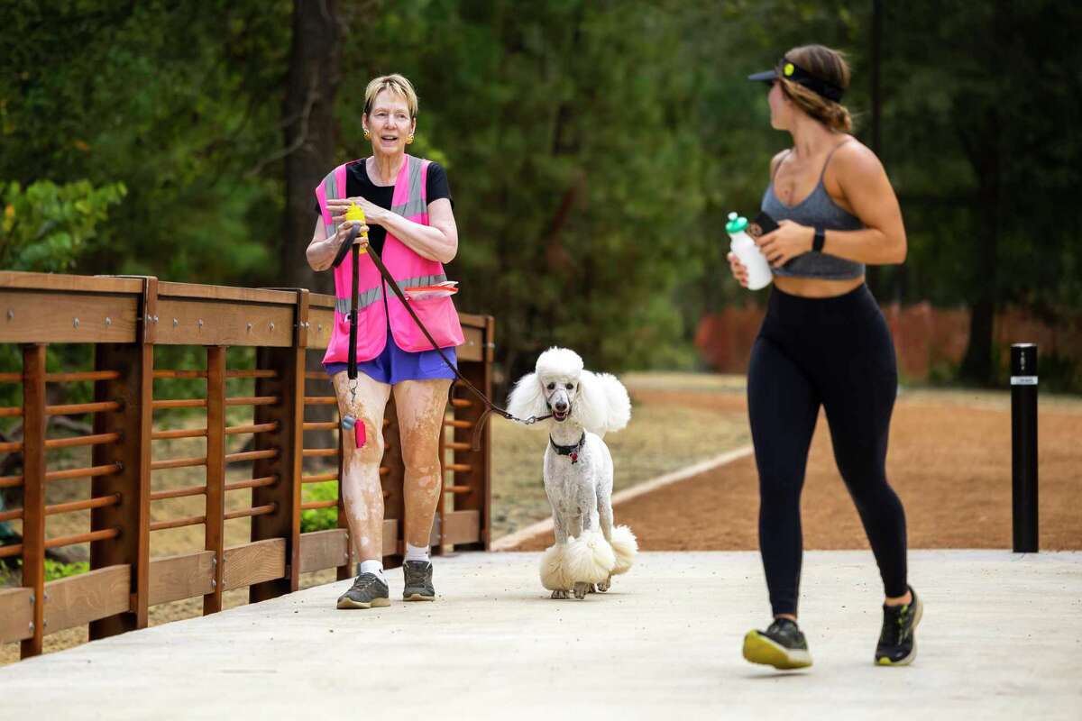 Marsha Schenau walks her pup, Joseph, during the opening of a new section of the Seymour Lieberman Trail at Memorial Park on Friday, Oct. 7, 2022. The newest section diverts runners off of the sidewalk along Memorial Drive to a new, shaded trail with three pedestrian bridges.