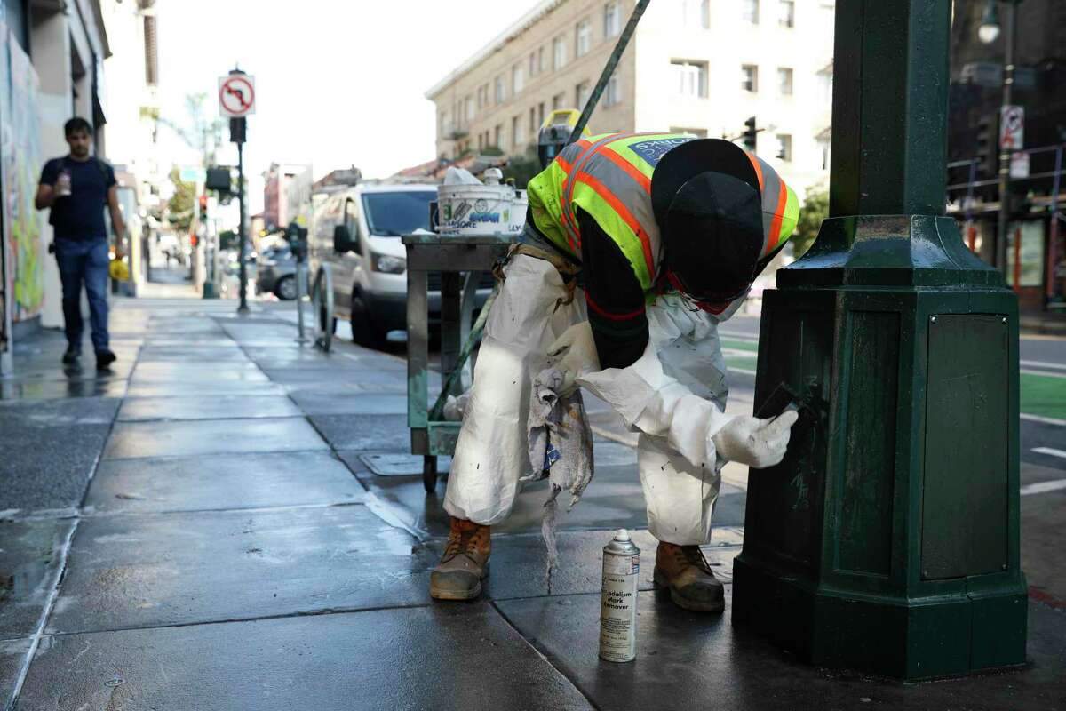 Frederick Johnson, Department of Public Works general laborer, cleans the graffiti on a lamppost on Polk Street as a San Francisco Public Works crew clean streets and sidewalks on Thursday, October 6, 2022 in San Francisco, Calif.