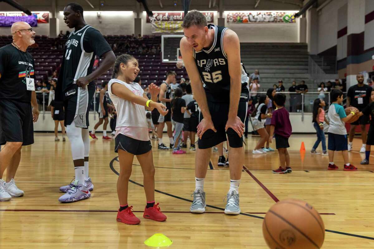 The Spurs’ Jakob Poeltl listens to an elementary student as they play together during a practice held Saturday at Uvalde High School's Harvey Kinchlow Gym.