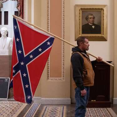 2021年1月6日，在美国首都华盛顿，特朗普总统的支持者凯文·塞弗里德在参议院议事厅外举着南方联盟旗帜。