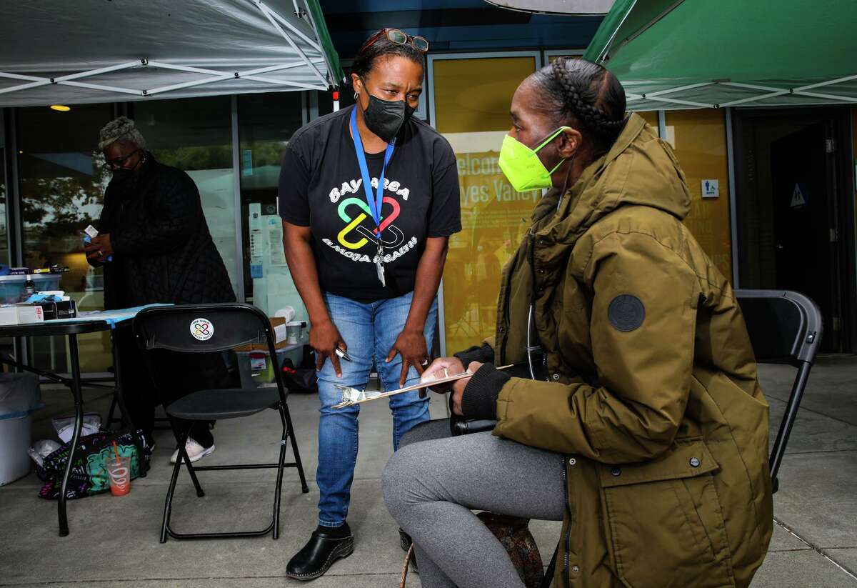 Dr. Kim Rhoads (center), founder of Umoja Health Partners, chats with community member Seana McGee during a health fair at Hayes Valley Playground in San Francisco. McGee was planning to receive a monkeypox vaccination and COVID-19 booster.