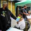 卡桑德拉·罗伯逊(左)和Umoja Health Partners于2022年10月12日星期三在加利福尼亚州旧金山海斯谷游乐场的健康博览会上为Seana McGee注射了COVID-19加强疫苗后，将创可贴贴在她的手臂上。