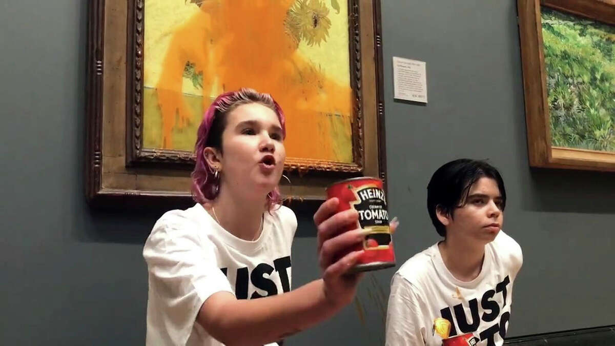 Handout photo issued by Just Stop Oil of two protesters who have thrown tinned soup at Vincent Van Gogh's famous 1888 work Sunflowers at the National Gallery in London, Friday Oct. 14, 2022. The group Just Stop Oil, which wants the British government to halt new oil and gas projects, said activists dumped two cans of Heinz tomato soup over the oil painting on Friday. London’s Metropolitan Police said officers arrested two people on suspicion of criminal damage and aggravated trespass. (Just Stop Oil via AP)