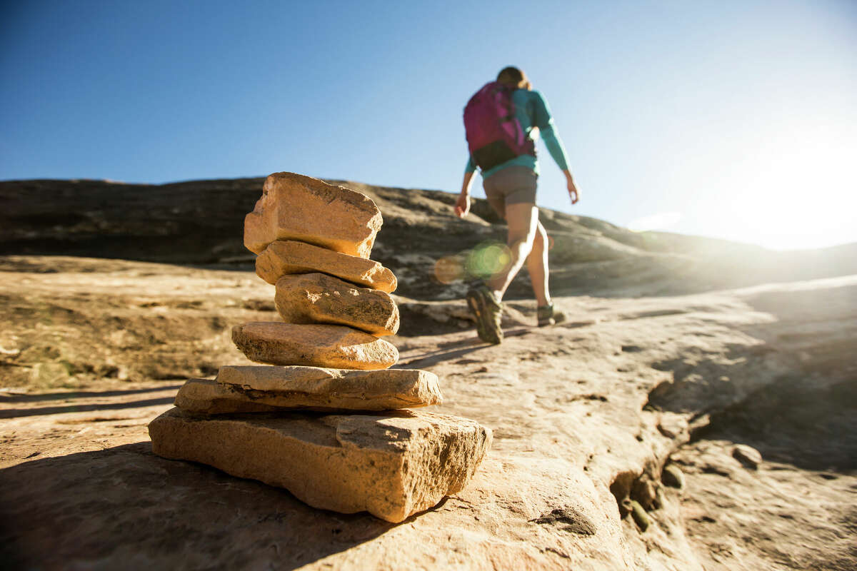 A young woman passing a cairn while hiking through The Needles at Canyonlands National Park in Utah.