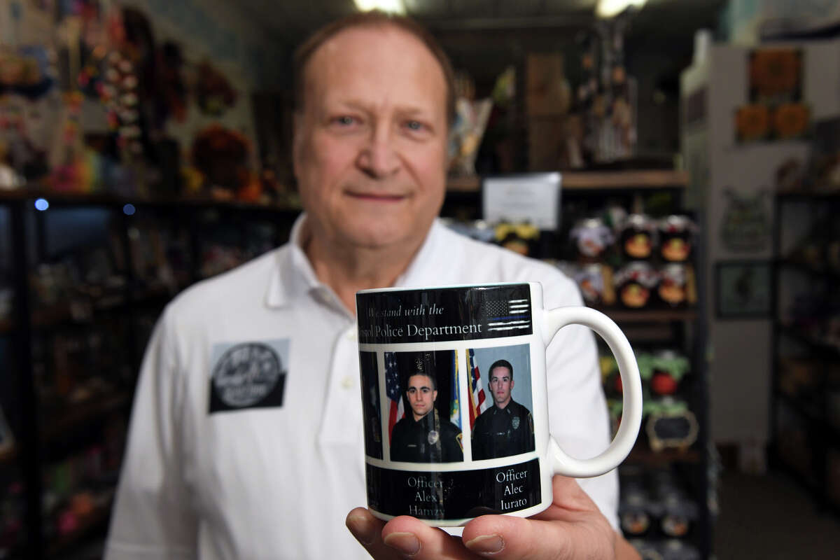 Bryan Lizotte, owner of Shelton Gift Boutique, holds one of the first 50 coffee mugs created and donated to Lights on Rosewood, in Bristol, in honor of slain Bristol Police officers Lt. Dustin Demonte and Sgt. Alex Hamzy, seen here in Shelton, Conn. Oct. 20, 2022.