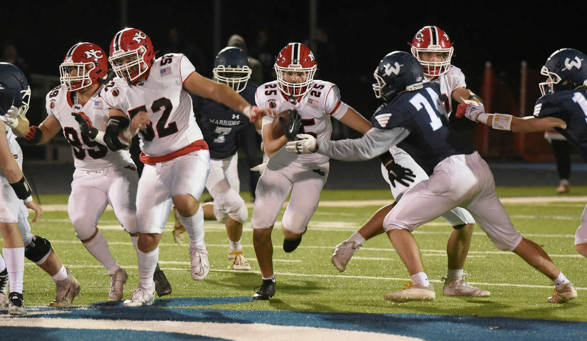 New Canaan's Luke Reed (25) runs through a hole in the line with blocking from Javier Soto-Perez (52) and Will Pepe (99) during a football game in Wilton on Friday, Oct. 21, 2022.