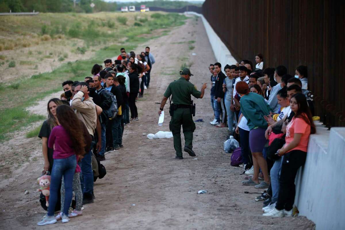 FILE - A group of migrants stand next to the border wall as a Border Patrol agent takes a head count in Eagle Pass, Texas, May 21, 2022. A surge in migration from Venezuela, Cuba and Nicaragua in September brought the number of illegal crossings to the highest level ever recorded in a fiscal year, according to U.S. Customs and Border Protection.
