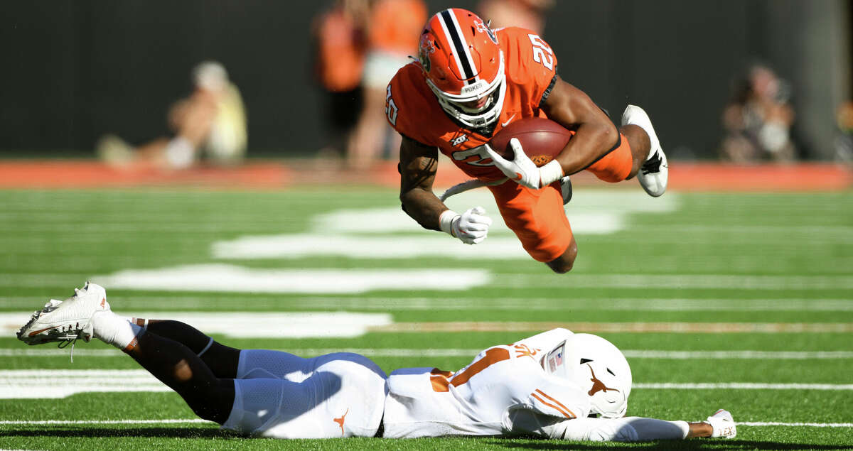 Oklahoma State running back Dominic Richardson (20) launches himself over Texas defensive back Anthony Cook, bottom, during the first half of an NCAA college football game Saturday, Oct. 22, 2022, in Stillwater, Okla. (AP Photo/Brody Schmidt)