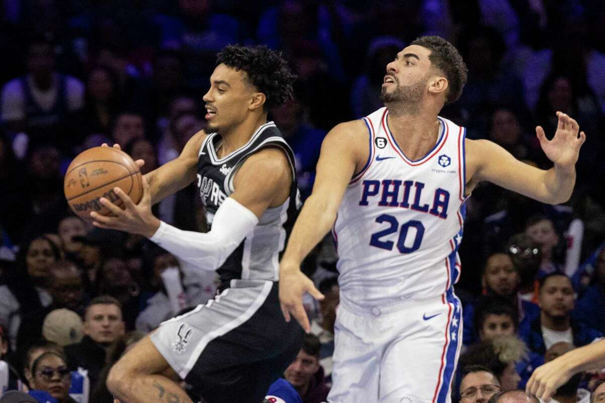 San Antonio Spurs guard Tre Jones (33) is followed to the basket by Philadelphia 76ers forward Georges Niang (20) during the second half of an NBA basketball game, Saturday, Oct. 22, 2022, in Philadelphia. (AP Photo/Laurence Kesterson)