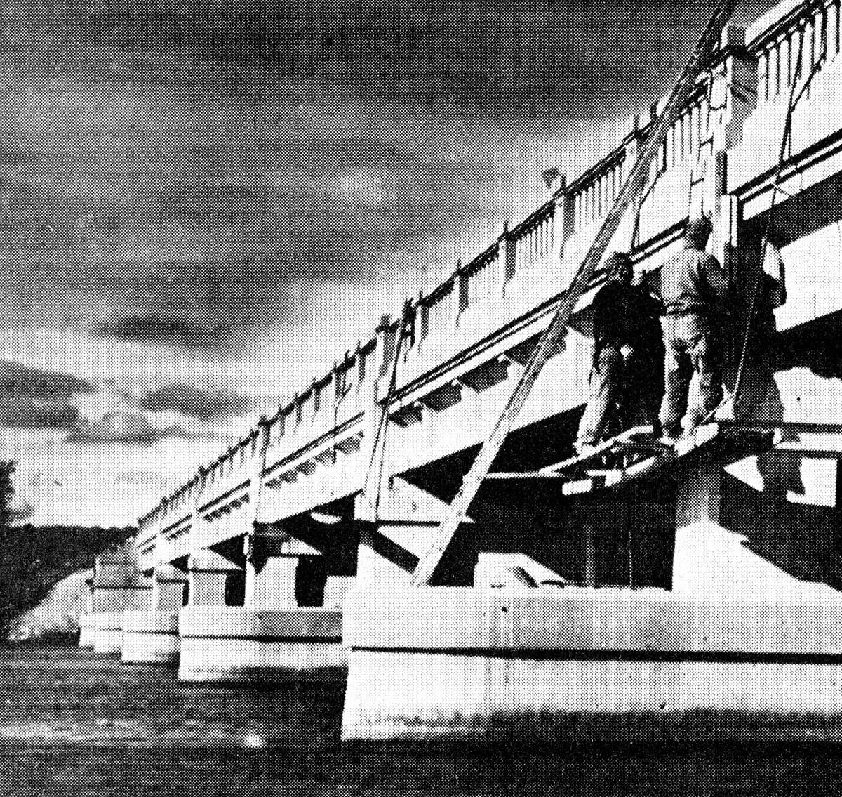 State highway department employees repair the support columns of the M-55 Bridge which crosses the Big Manistee River. The concrete facings on some of the columns have broken up, requiring repair work. The job is expected to be completed by the end of the month. The photo was published in the News Advocate on Oct. 26, 1962.