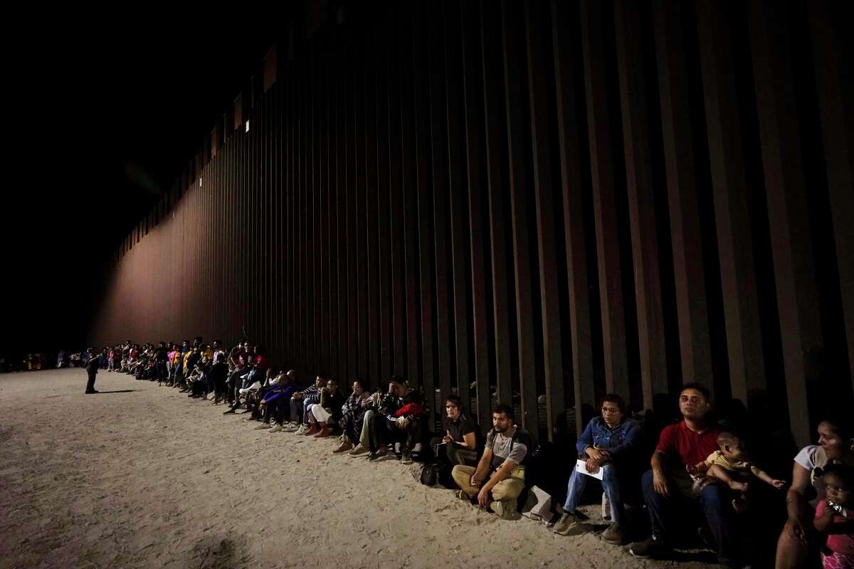 Migrants wait along a border wall Aug. 23, 2022, after crossing from Mexico near Yuma, Ariz.