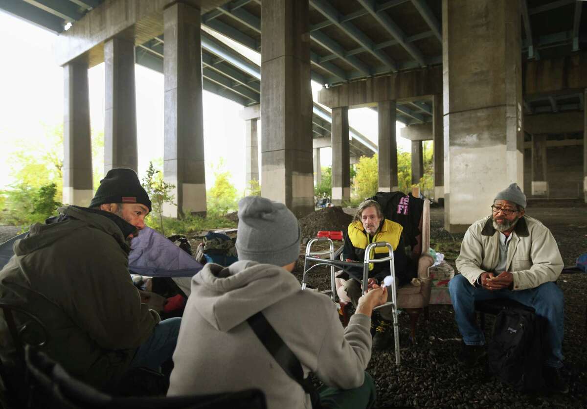 From left; Luis Maldonado, Juan Soto, Richard Martinez, and George McClain talk in a circle in their homeless encampment beneath the I-95 overpass on Kossuth Street in Bridgeport, Conn. on Wednesday, October 26, 2022. 