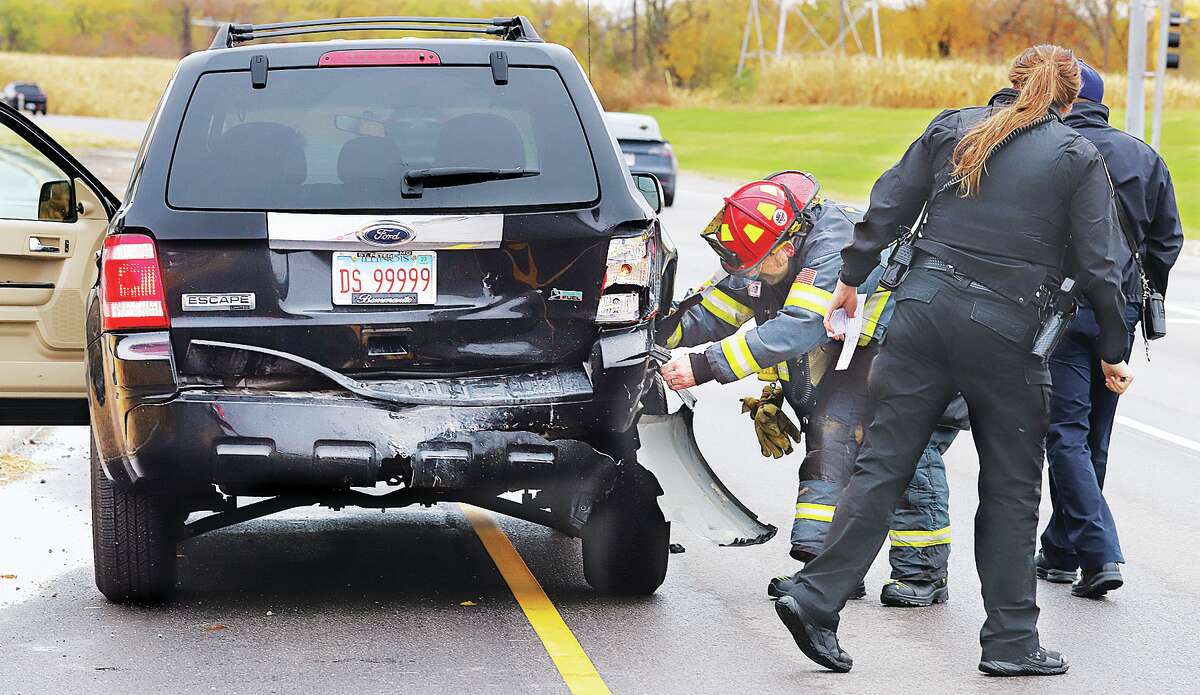 John Badman|The Telegraph An Alton Fire Department captain pulls warped plastic back over the rear wheel of a Ford Escape involved in a Tuesday crash on College Avenue near the Powder Mill Road.