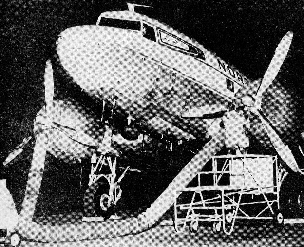 Overnight wraps are fastened to the North Central Airlines DC-3 engines by station agent Dave Abbott after arriving from Grand Rapids at 8:33 p.m. The DC-3 is based overnight in Manistee ensuring passengers on the early morning flight almost certain departure under reasonable conditions. The photo was published in the News Advocate in Oct. 30, 1962.